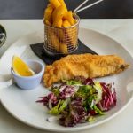 Close-up of traditional fish and chips with fresh salad served on a white plate.